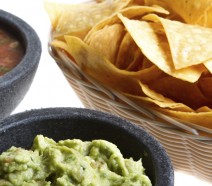 Close shot of fresh Mexican corn chips in a wicker basket, homemade spicy salsa and gourmet guacamole from a nice Mexican restaurant isolated on white