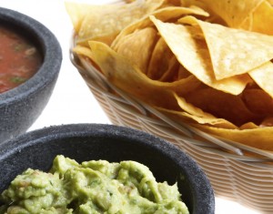 Close shot of fresh Mexican corn chips in a wicker basket, homemade spicy salsa and gourmet guacamole from a nice Mexican restaurant isolated on white